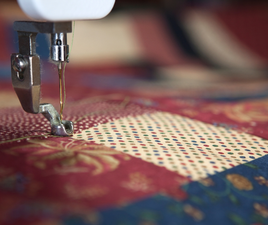 Close up of sewing machine quilting a burgundy and blue quilt